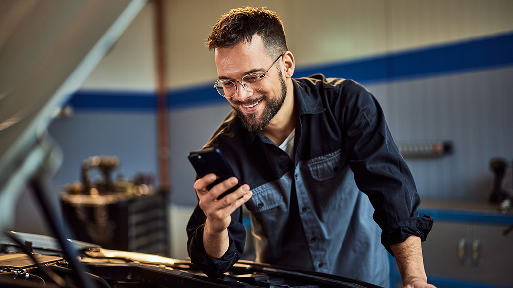 Mechanic leaning on car looking at mobile phone