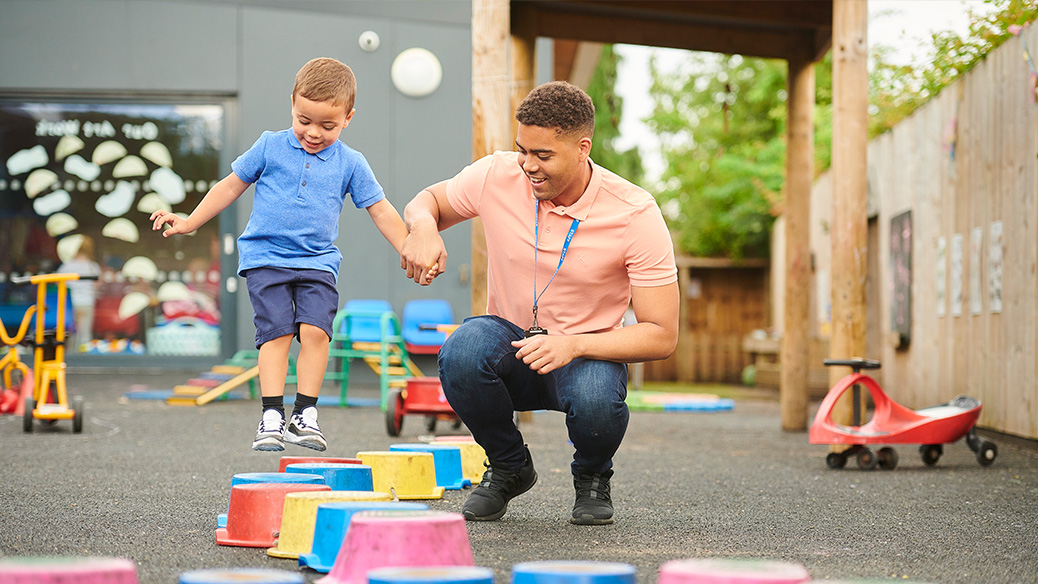 Child care worker helping a child to balance as they walk on obstacles